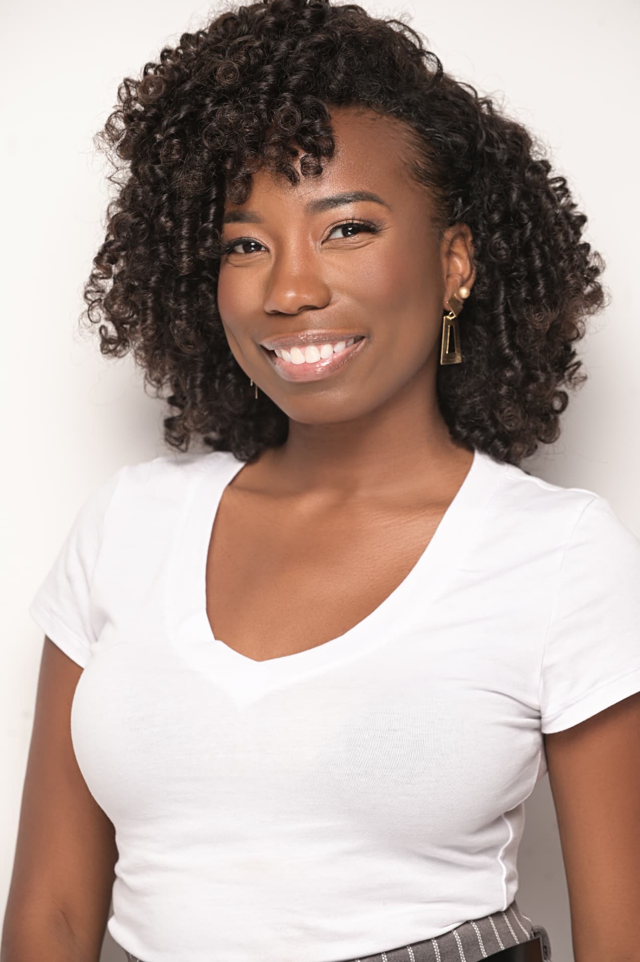 Close portrait of Zarah Charm smiling in a white t-shirt against a soft grey backdrop